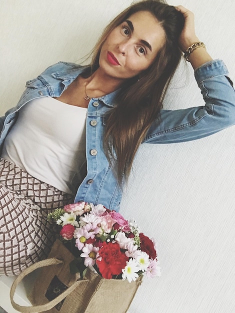 Photo portrait of young woman with flowers sitting against wall