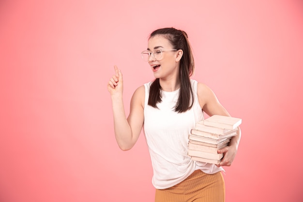 Portrait of a young woman with glasses on a pink background with books in her hands .