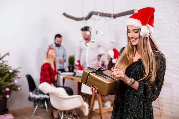 Portrait of a young woman with a gold giftbox at home on the foreground beautiful blonde in a santa ...