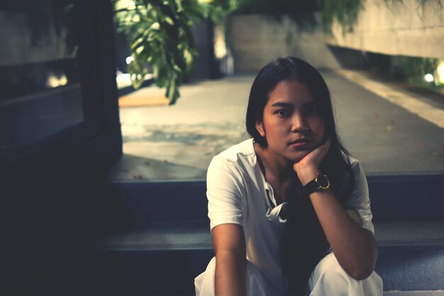 Photo portrait of young woman with hand on chin sitting on steps at night