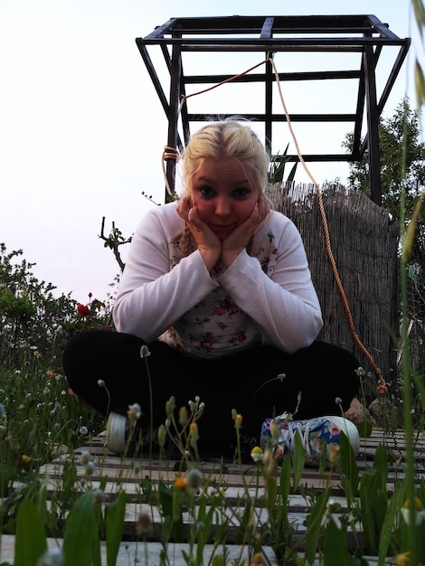 Photo portrait of young woman with hands on cheek sitting by plants