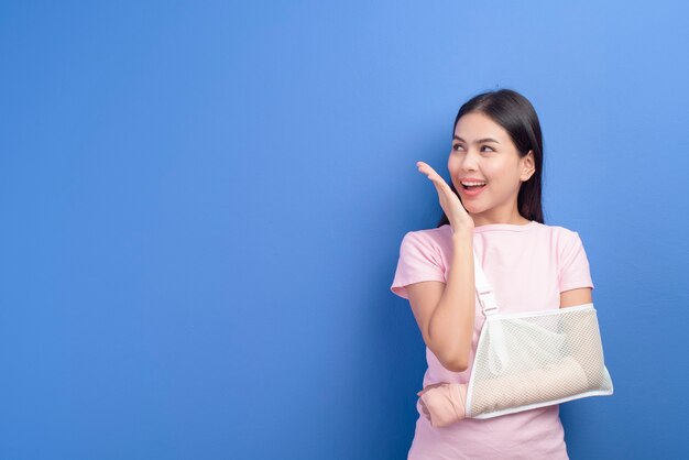 A portrait of young woman with an injured arm in a sling over blue wall