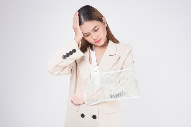 Portrait of young woman with an injured arm in a sling over white background in studio.