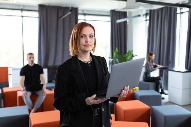 Portrait of a young woman with a laptop against the background of colleagues working in the office