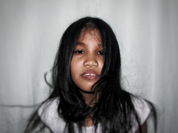 Photo portrait of young woman with long black hair against white curtain