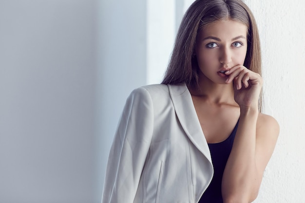 Foto ritratto di giovane donna con lunghi capelli castani in maglietta nera e giacca bianca.