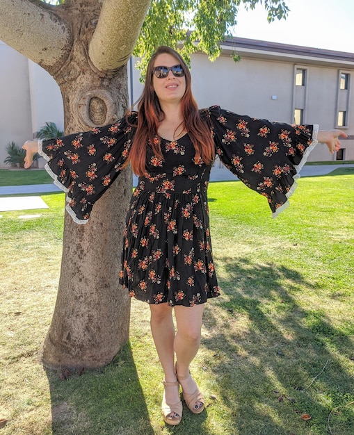 Photo portrait of young woman with long red hair wearing a boho dress and arms spread standing outdoors