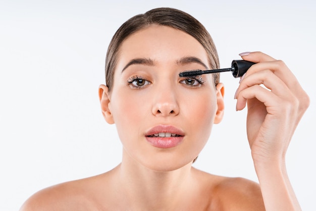 Portrait of young woman with makeup brush applying black mascara