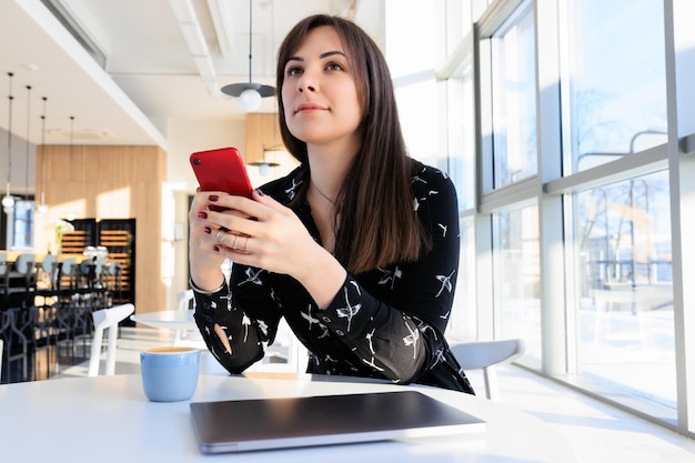 スタイリッシュな街のカフェで携帯電話を持つ若い女性の肖像画