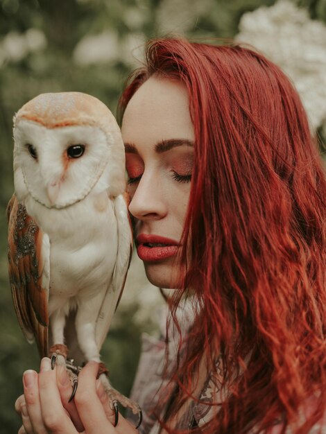 Portrait of young woman with red hair in a lilac garden with an owl barn owl