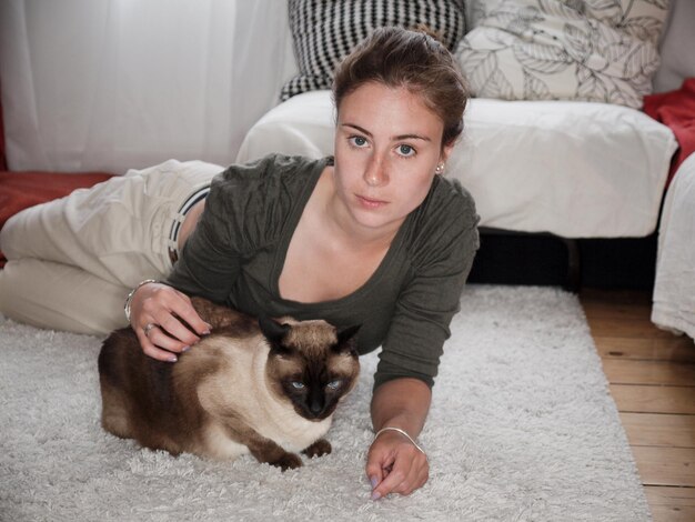 Photo portrait of young woman with siamese cat on carpet at home