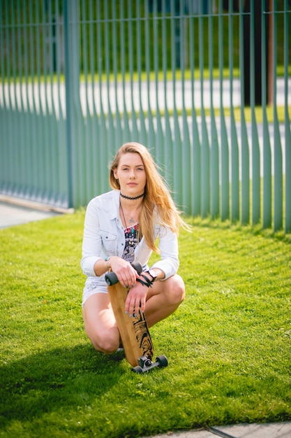 portrait of young woman with skateboard crouching in park