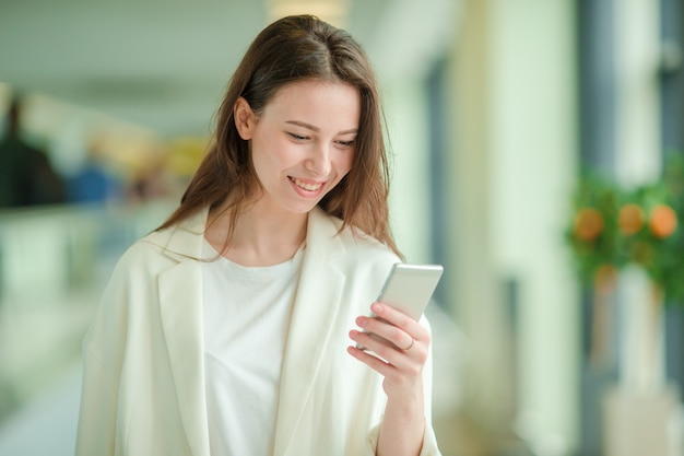 国際空港でスマートフォンを持つ若い女性の肖像画。飛行機を待っている空港ラウンジの航空会社の乗客