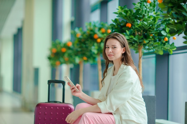 国際空港でスマートフォンを持つ若い女性の肖像画。飛行機を待っている空港ラウンジの航空会社の乗客