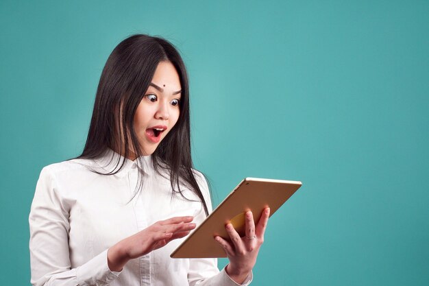 Portrait of a young woman with a surprised expression looks at a tablet in the Studio on an isolated background