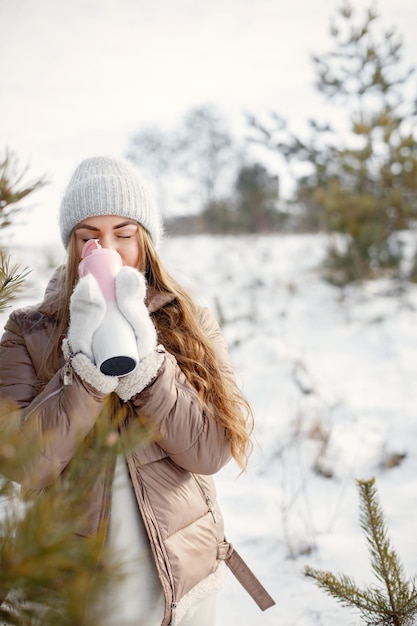 Portrait of a young woman with thermos standing in forest at winter day