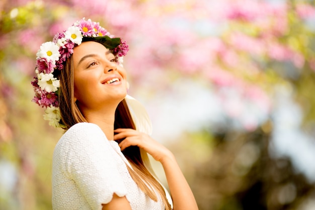 Portrait of young woman with wreath of fresh flowers on head in the park