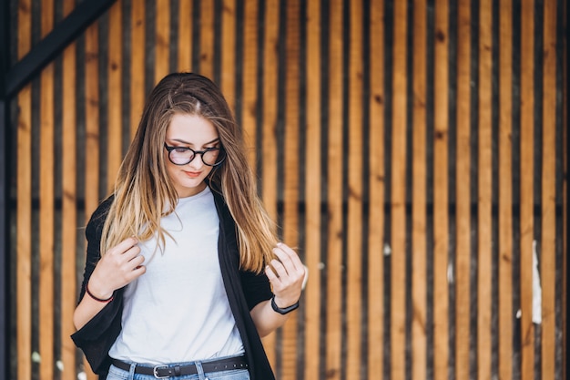 Portrait of a young woman on the wooden background with vertical boards. Beautiful girl with long hair and glasses smiling