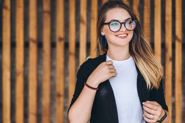 Portrait of a young woman on the wooden background with vertical boards. Beautiful girl with long hair and glasses smiling