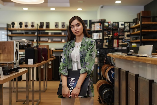 Portrait of young woman working in music store amd holding vinyl record looking at camera copy space