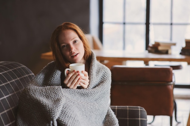 Photo portrait of young woman wrapped in blanket holding coffee cup on sofa at home