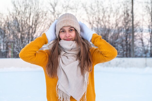 Portrait of young woman in yellow sweater skating at the rink looking at camera