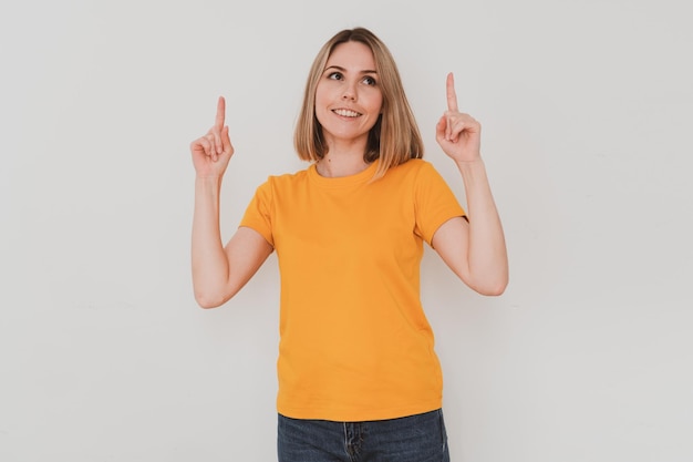 Portrait of young woman in yellow t-shirt pointing her finger up. On white background. Hand gestures