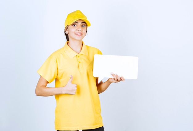 Portrait of a young woman in yellow uniform with an empty speech bubble showing a thumb up . 