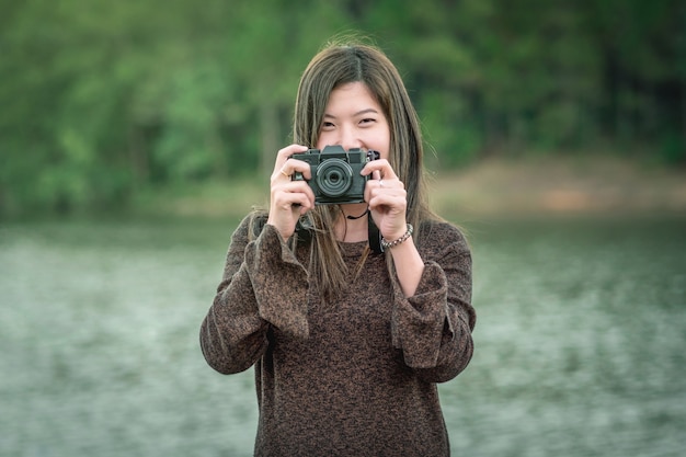 湖の背景と森の上で若い女性の写真家の肖像画