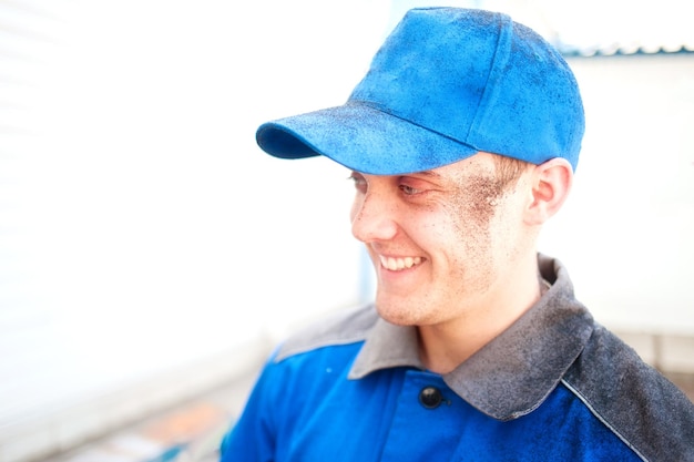 Portrait of young worker in work clothes and blue baseball cap with stained face Positive emotions