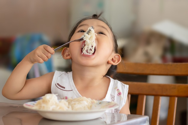 Портретное изображение 3-4-летнего ребенка. Счастливая азиатская девочка-ребенок любит есть немного лапши от Сама. Концепция здорового питания и детей.