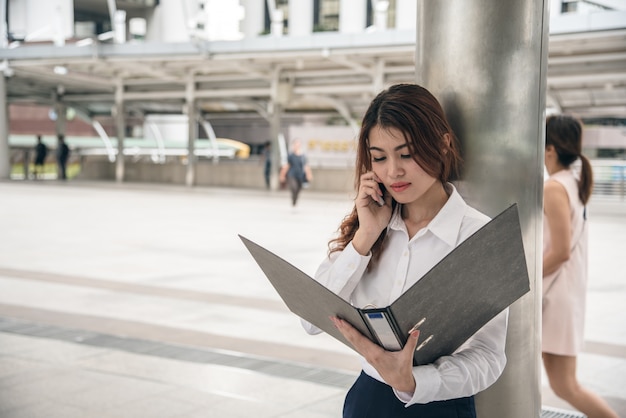 美しいアジアの女性の肖像画が自信を持って立って、携帯電話を保持している