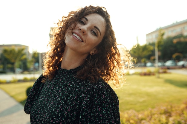 Portraits of a charming red-haired girl with freckles and a pretty face. The girl poses for the camera in the city center. She has a great mood and a sweet smile