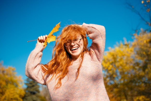 Фото Портреты очаровательной рыжеволосой девушки с симпатичным лицом. девушка позирует в осенний парк в свитер и коралловые юбки. в руках у девушки желтый лист