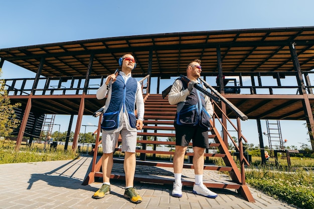 Portraits of two adult mans in sunglasses protective headphones and a rifle vest