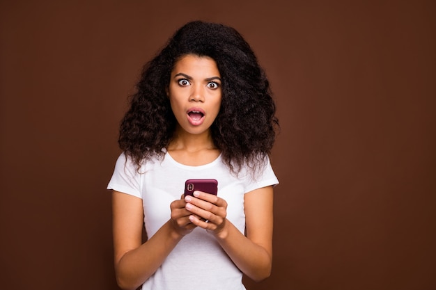 驚いたショックを受けたアフリカ系アメリカ人の女の子の肖像は、携帯電話を使用してソーシャルネットワーク情報を読んで、スタイリッシュな服を着て悲鳴を上げるのだろうか。