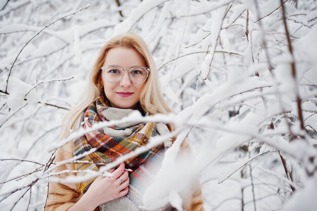 Portraiy of blonde girl in glasses, red fur coat and scarf at winter day.