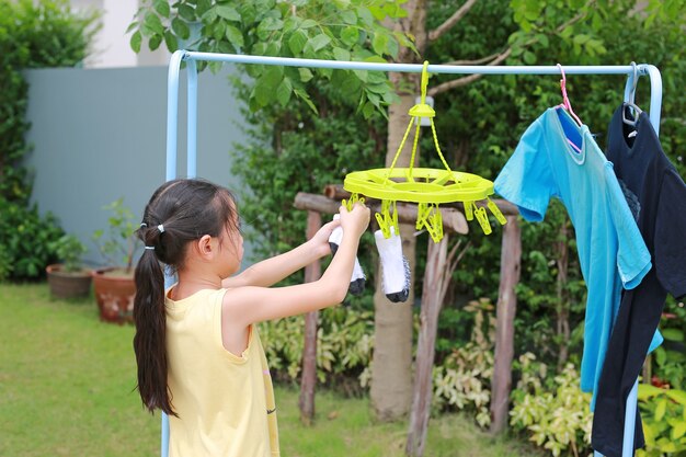 Portret aziatisch klein meisje dat wasknijper zet en sokken ophangt om kleren te drogen. kind doet de was in de tuin
