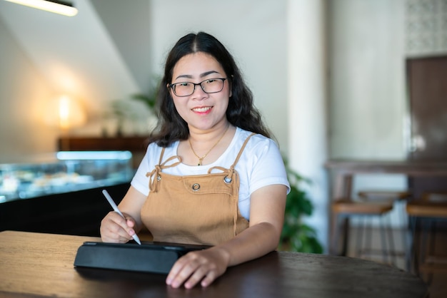 Portret aziatische freelance mensen zakenvrouw dragen van een bril stijlvolle hipster tekenen of notities maken op digitale tablet met elektronische pen voor surfen op internet, chatten en bloggen in de coffeeshop