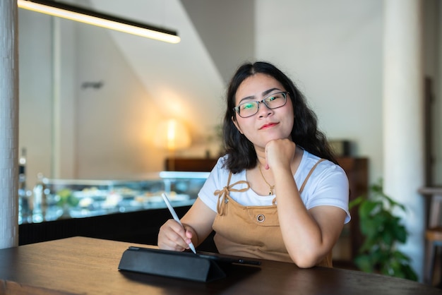 Portret Aziatische freelance mensen zakenvrouw dragen van een bril stijlvolle hipster Tekenen of notities maken op digitale tablet met elektronische pen voor surfen op internet, chatten en bloggen in de coffeeshop