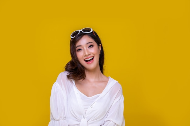 Portret Aziatische mooie gelukkige jonge vrouw die vrolijk glimlacht en camera bekijkt die op gele studioachtergrond wordt geïsoleerd