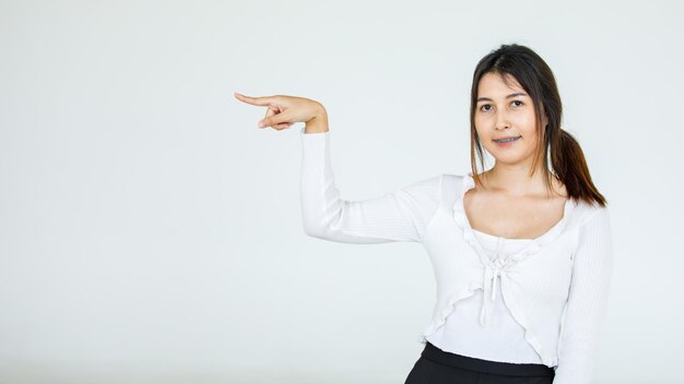 Portret Aziatische mooie vrouw draagt casual shirt staande poses, wijzende advertentie op witte achtergrond, lege kopie ruimte met een geïsoleerde lachende blik op de camera.