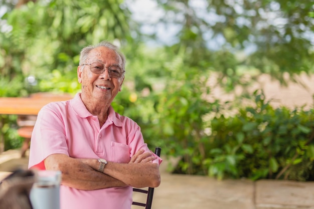 Portret Aziatische oudere man van 83 jaar oud met een brede glimlach die buiten in de tuin zit