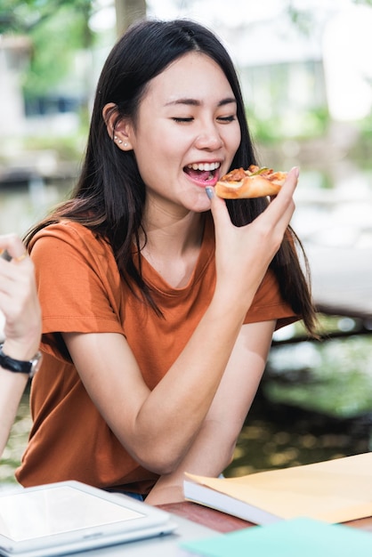 Portret aziatische studentes die pizza met heerlijke kaas eten bij openluchtuniversiteit, Onderwijsconcept