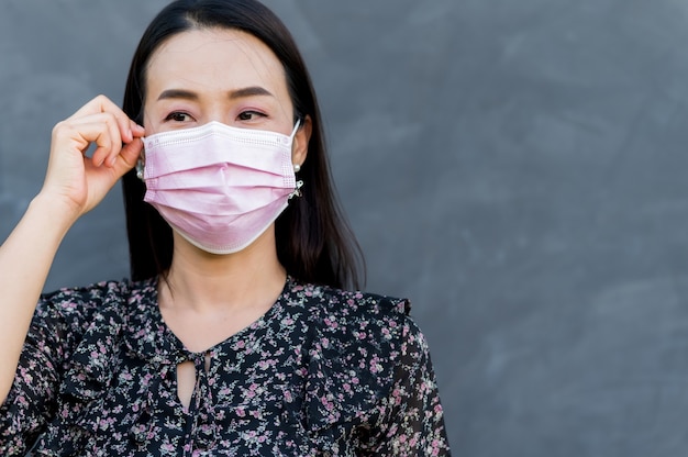 Portret aziatische vrouw dragen gezichtsmasker met kale cement oppervlak