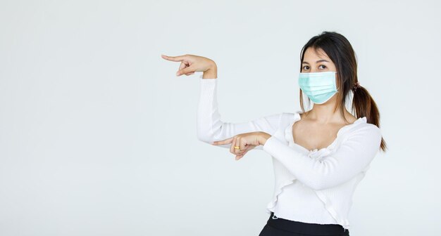 Portret Aziatische vrouw met een gezichtsmasker poseert, wijzend op advertentie op witte achtergrond, lege kopieerruimte met geïsoleerde witte achtergrondknipsel.