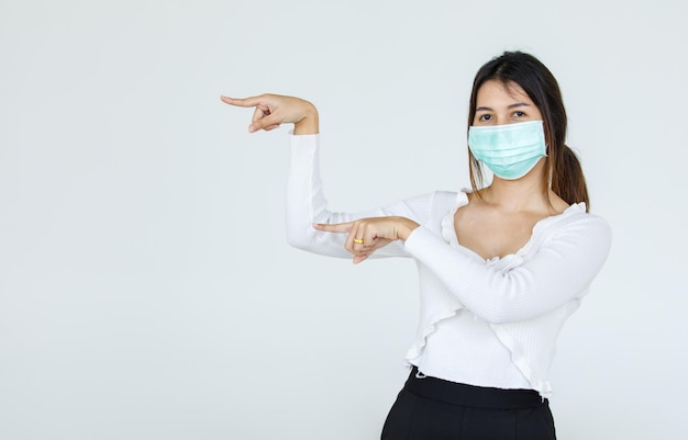 Portret Aziatische vrouw met een gezichtsmasker poseert, wijzend op advertentie op witte achtergrond, lege kopieerruimte met geïsoleerde witte achtergrondknipsel.