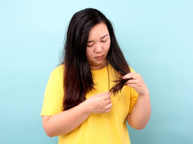 Portret aziatische vrouw met haarproblemen - broos, beschadigd, droog, vuil en verlieshaar, op blauwe achtergrond in studio.