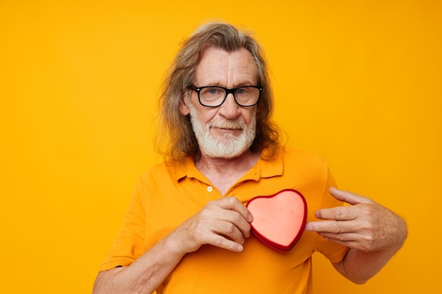 Portret bejaarde man gele t-shirt en bril poseren hartvormige doos bijgesneden weergave