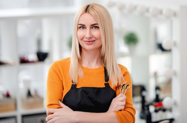 Portret of blond woman hairdresser smiling and holding in her hand scissors